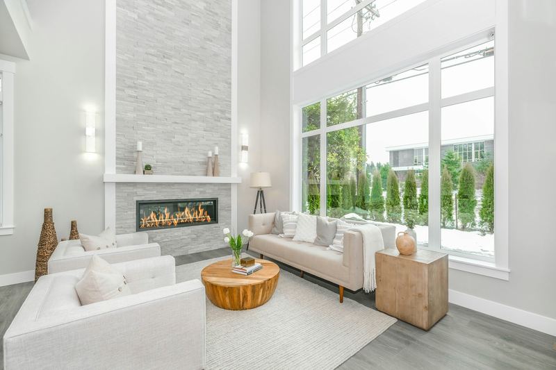 Airy two-story living room with a wall of tall windows, light sofas and a fireplace