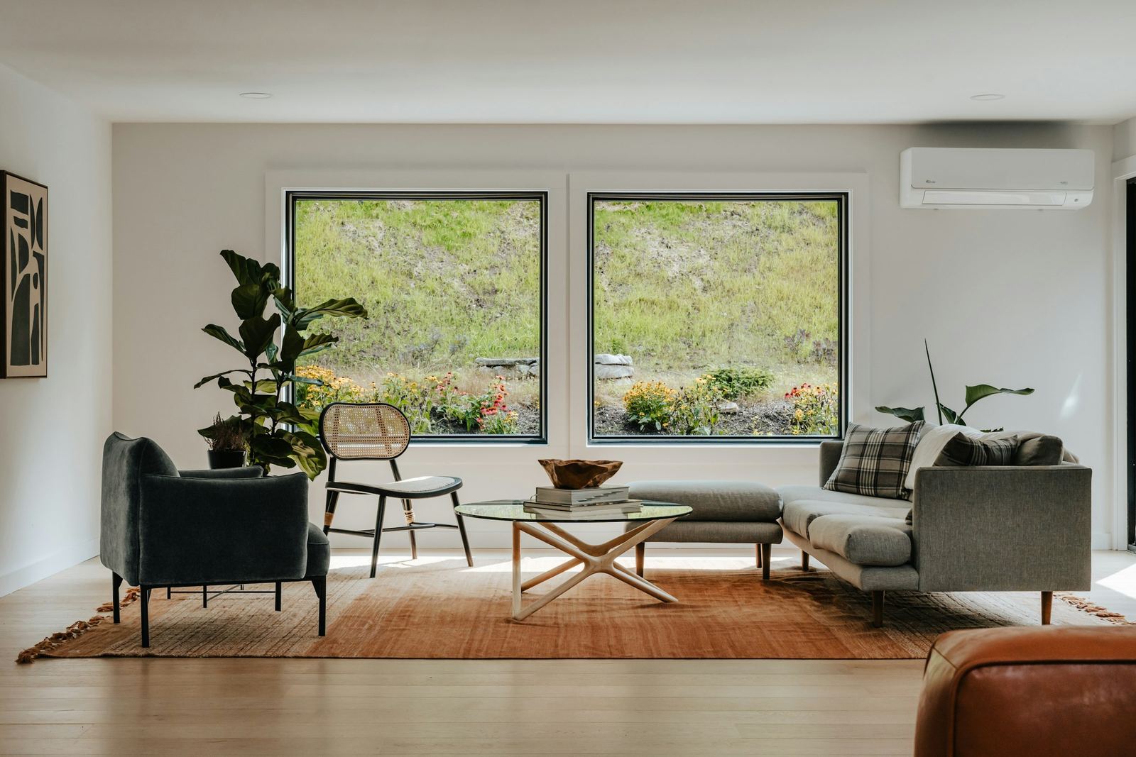 Bright living room with two large, spotless windows looking out on a green hillside garden