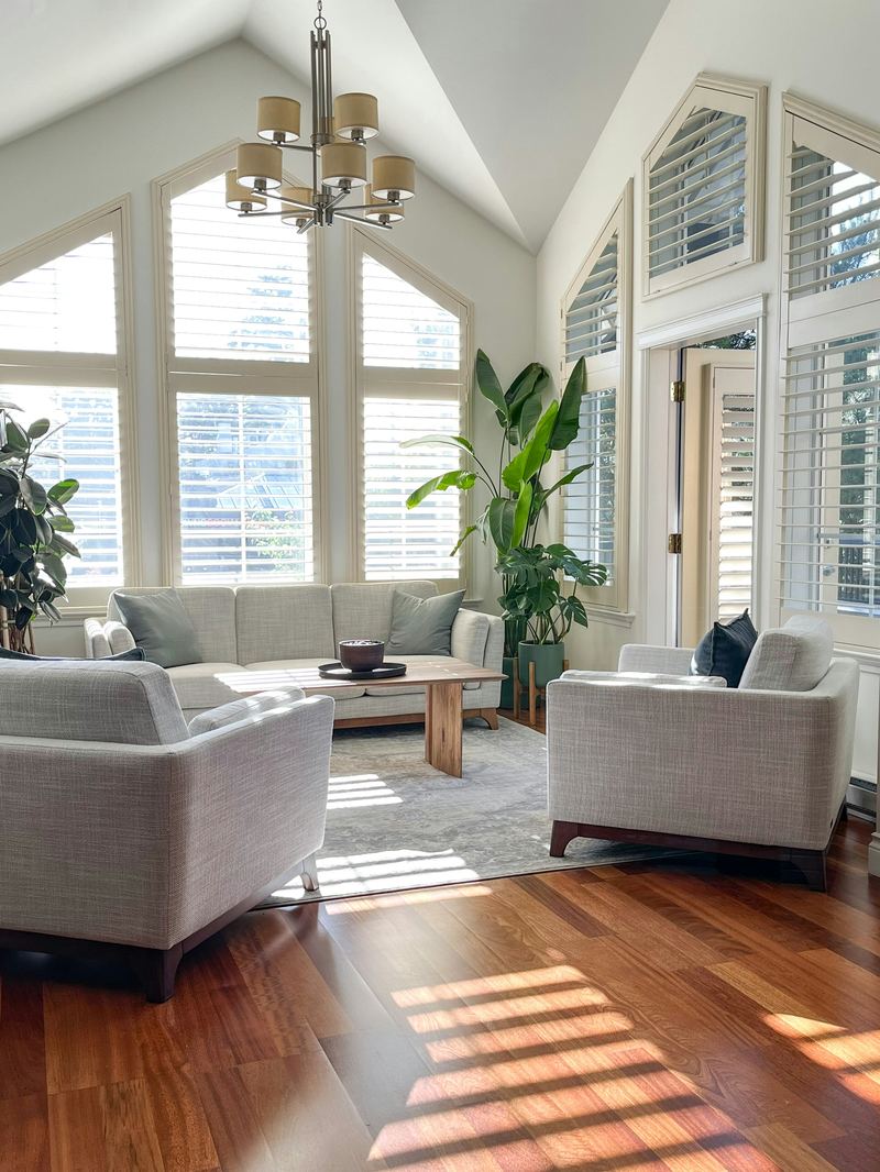 Sunlit living room with tall shuttered windows and a vaulted ceiling